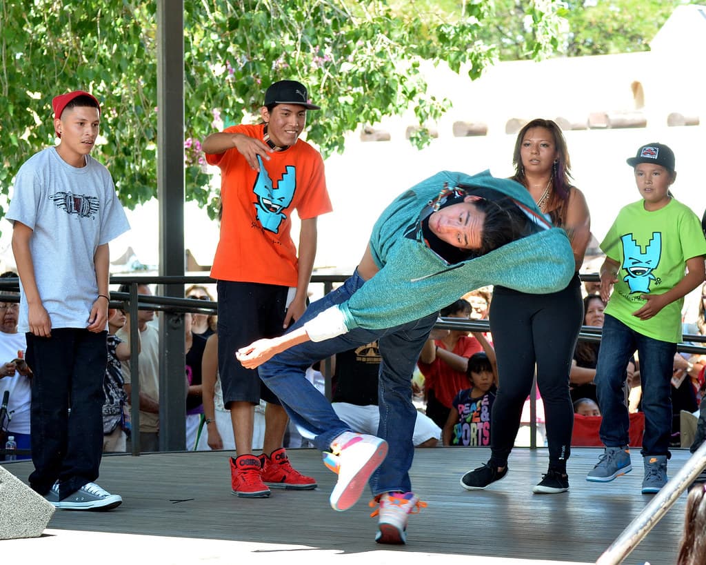 A young dancer performs a backbend on an outdoor stage while others watch at the Santa Fe Indian Market