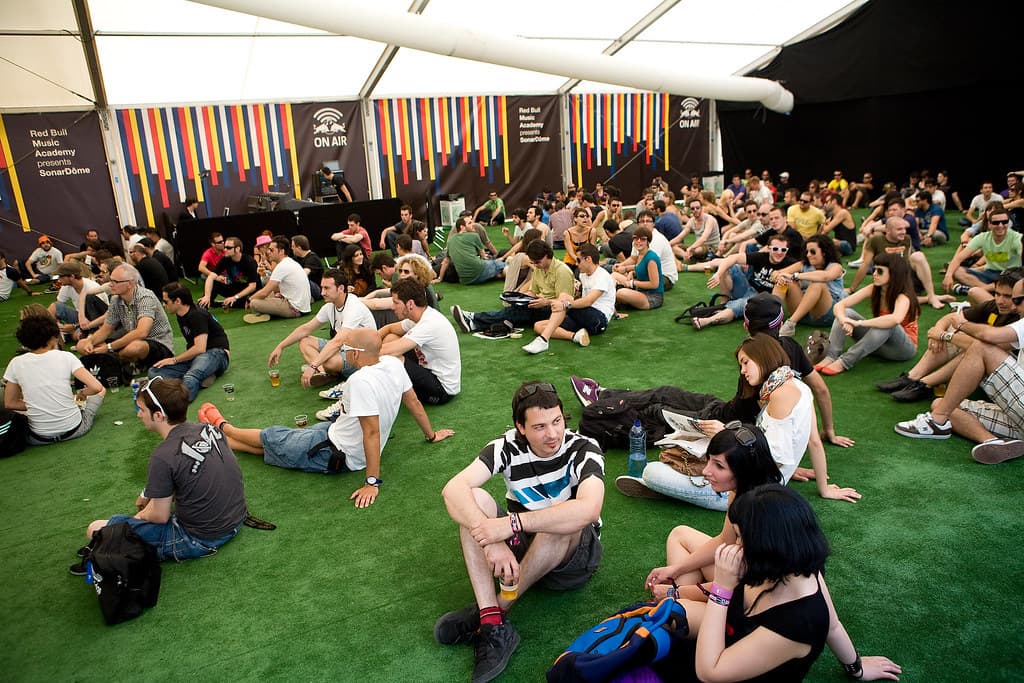 Festival-goers sit and relax on artificial grass under a big tent at Sónar by Day in Barcelona