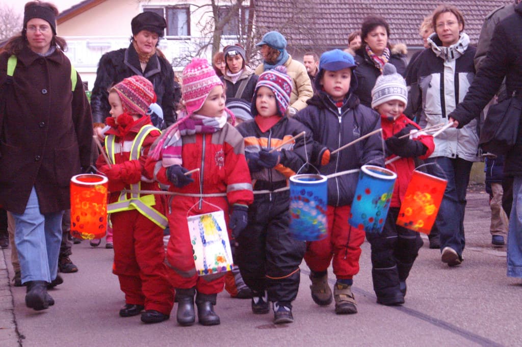 Children in winter coats carry glowing paper lanterns in a St. Martin's procession