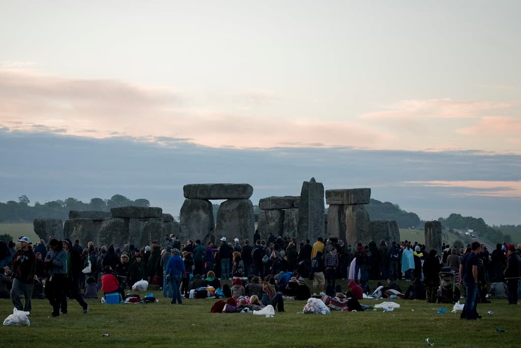 Crowds stand around the stones of Stonehenge under a pale dawn sky on the summer solstice