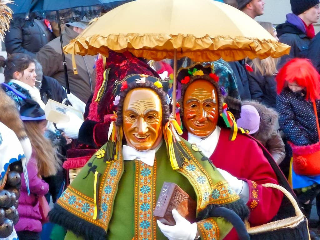 Masked Fasnet figures in painted wooden masks and embroidered costumes walk under parasols in Rottweil