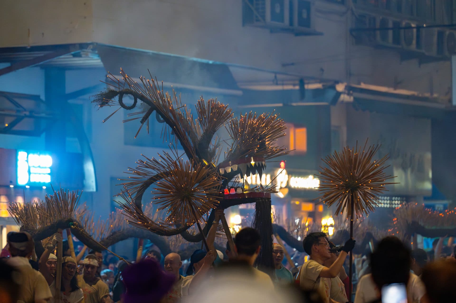 A dragon made of burning incense sticks rears above a crowd of carriers in a smoky Hong Kong street at night