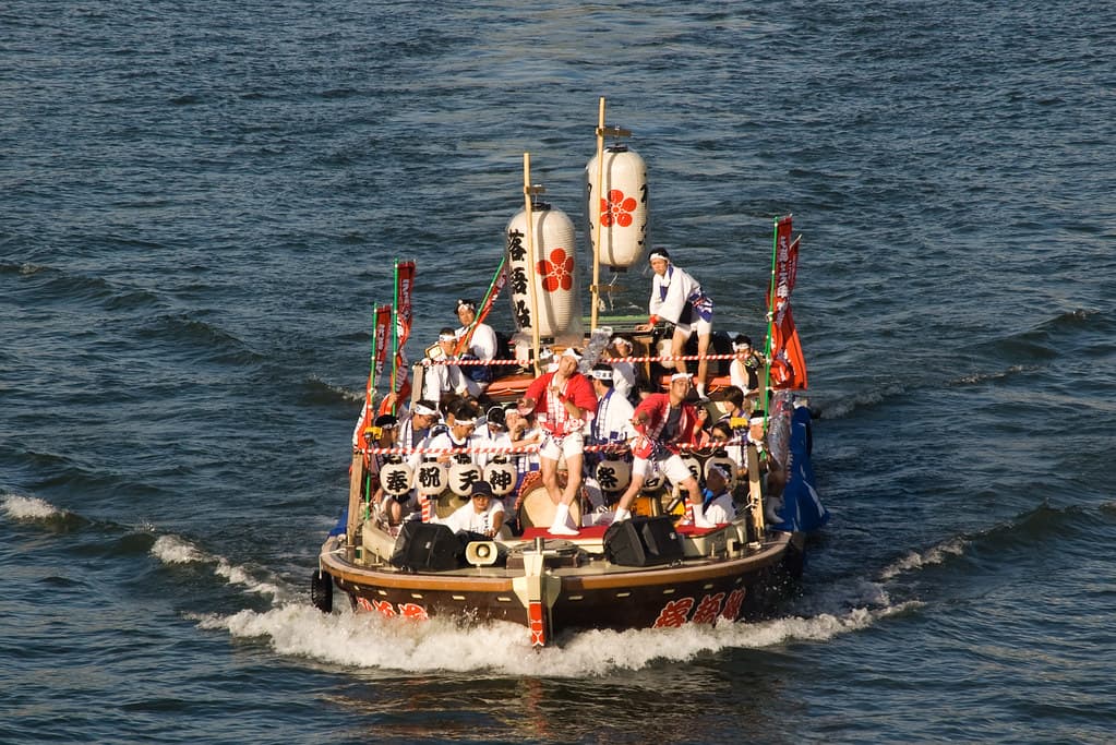 A festival boat with paper lanterns and dozens of people in white robes crosses the water