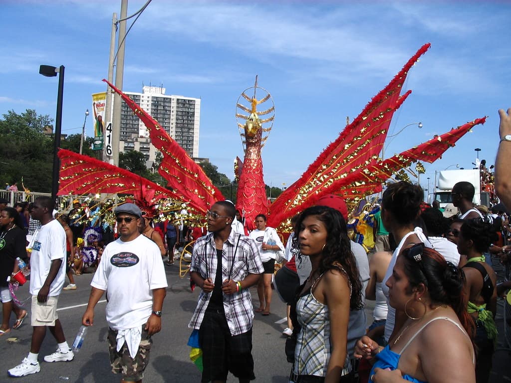 A masquerader in a huge red feathered costume with wings dances on Lake Shore Boulevard during the Toronto Caribbean Carnival