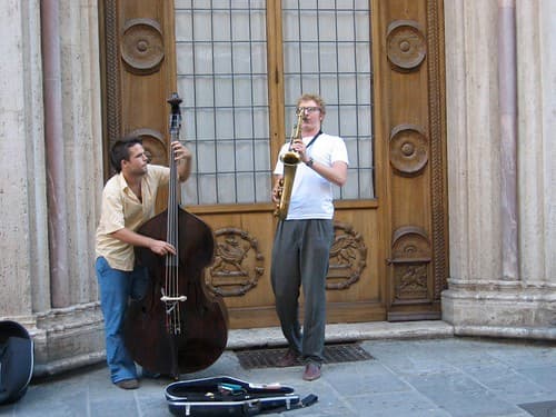 Two street musicians play double bass and saxophone in front of an ornate doorway in Perugia during Umbria Jazz