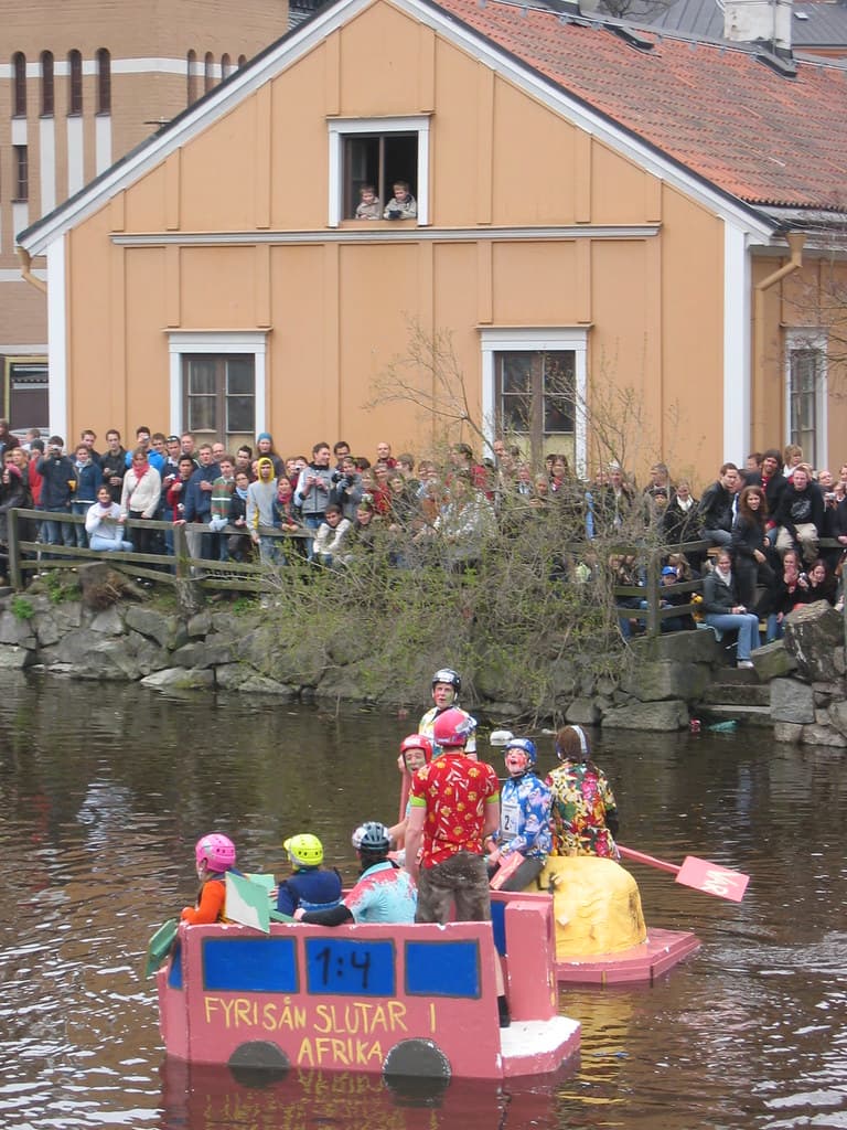 A home-made raft carrying students in costume floats down the Fyris River past crowds on the bank in Uppsala