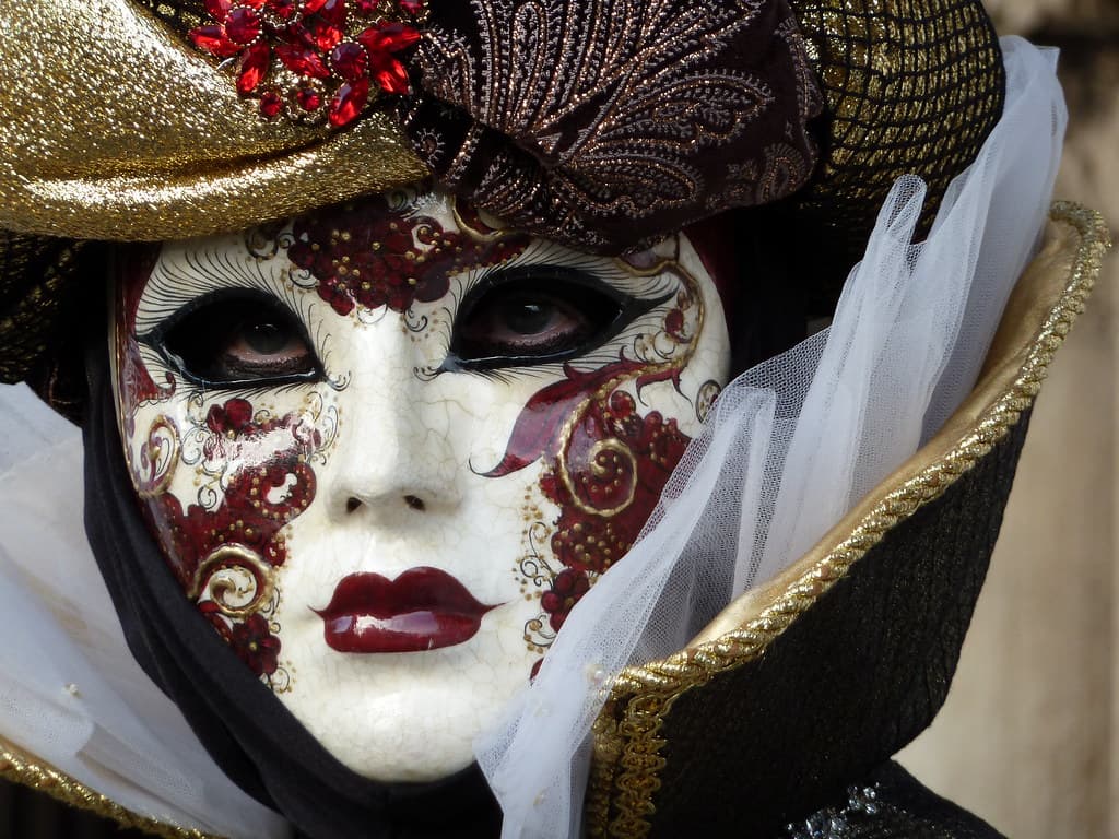 A white and burgundy ornate carnival mask close up