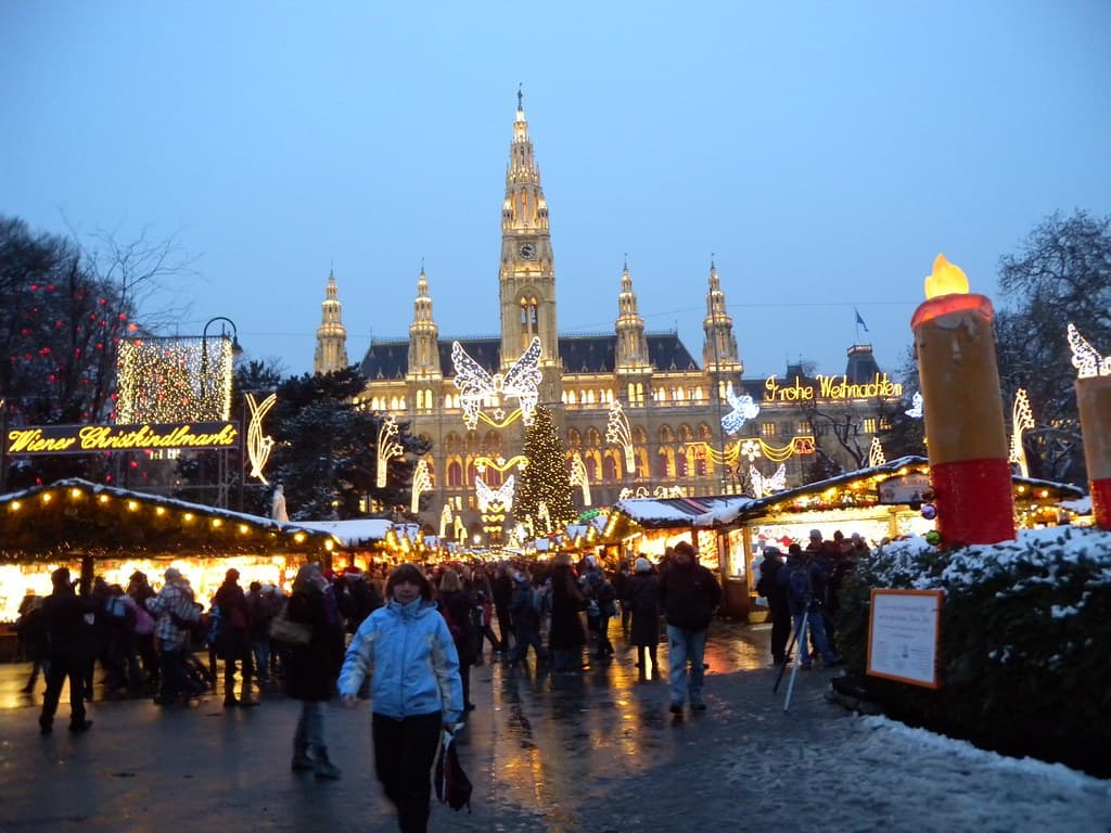 The lit-up Vienna City Hall towering over the Christkindlmarkt stalls on a snowy evening