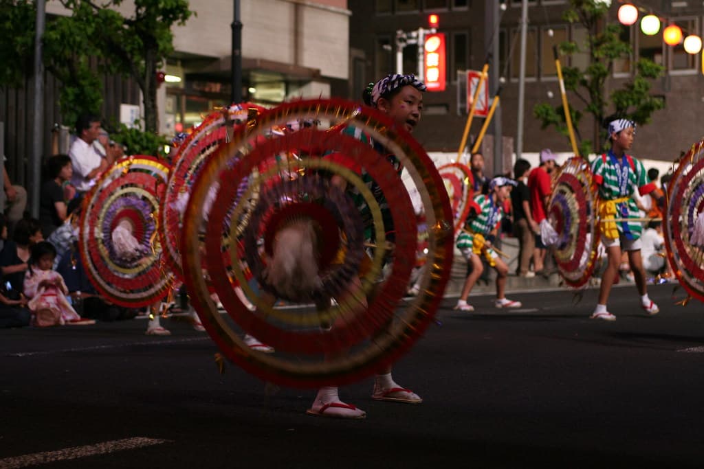 Dancers in costume spin red and yellow flower hats on a street at night during the Hanagasa Matsuri in Yamagata